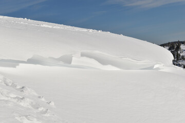 Obraz premium Große Schneeverwehung, Schneewechte hängt über tief verschneiter Fläche vor blauem Himmel im Gebirge