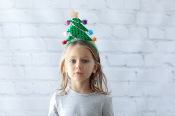 child girl in headband with a Christmas tree isolated white brick wall background.Happy new year
