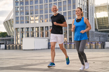 Cheerful mature couple, man and woman exercising and jogging together in the city on a warm summer...