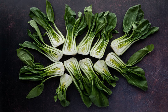 Top down view of an arrangement of bok choy clusters against a dark background.