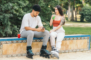Couple using mobile while drinking soft drink in a park with inline skates on