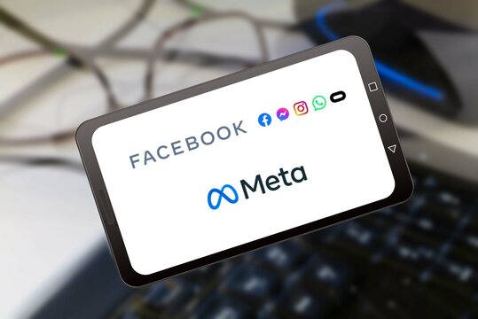 Germany, 11-2021: Meta the new facebook name logo on phone screen stock image. Background with blurred keyboard, mouse and glasses
