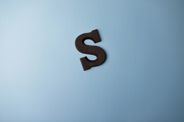 Letter of the alphabet S is made of dark milk chocolate on blue background.