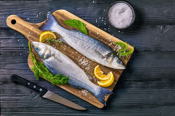 Raw sea bass a black wooden table, top view