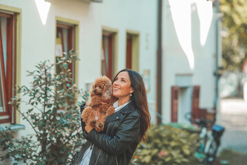 A young beautiful woman with her poodle dog is walking in a European city. Happiness. Little pet.