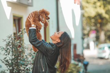 A young beautiful woman with her poodle dog is walking in a European city. Happiness. Little pet.