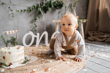 Fototapeta premium Pretty baby first year birthday, toddler with cake on the floor, rustic style decoration.