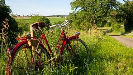 Fototapeta na wymiar Vieux vélo rouge en bord de chemin sur une route de campagne.