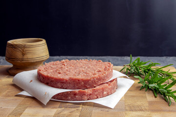 Fresh raw homemade beef burger cutlets on a cutting board with spices and herbs.