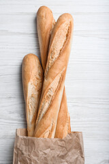 Tasty baguettes in package on white wooden table, top view