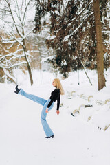 Stylish blonde in baggy jeans posing in a winter park.