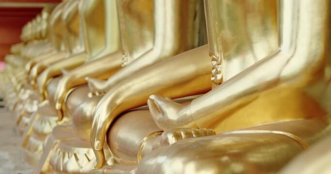 Rack focus and dolly in scene of golden Buddha statues lined up in a Buddhist temples in Thailand.