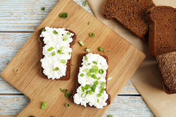 Obraz na płótnie Canvas Bread with cottage cheese and green onion on light blue wooden table, flat lay