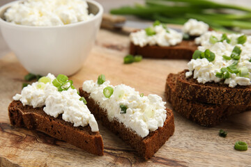 Bread with cottage cheese and green onion on wooden table, closeup