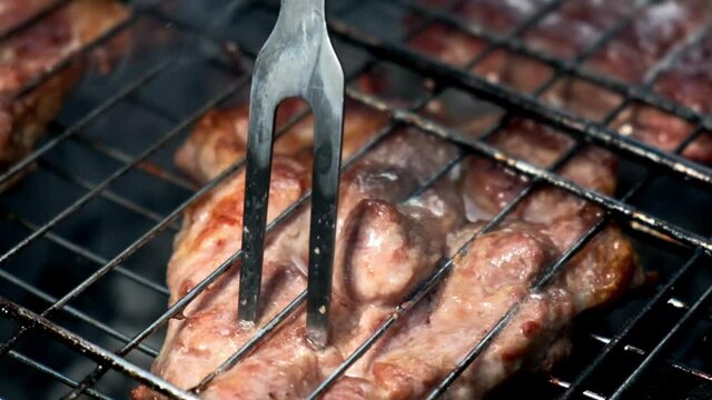 Meat prepared on grill. Fried juicy steak from pork meat inserted with special fork on iron grid above hot smoky brazier at picnic closeup