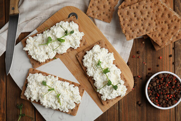 Crispy crackers with cottage cheese and microgreens on wooden table, flat lay