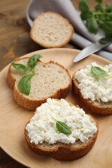 Bread with cottage cheese and basil on wooden plate, closeup