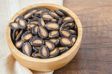 Black dry watermelon seeds in wooden bowl.