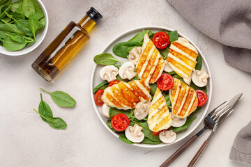 Vegetarian salad with spinach leaves, cherry tomatoes, mushrooms and grilled halumi cheese in a plate on the table. Top View