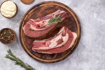 Several pieces of raw beef brisket on the bone with cranberries, rosemary and cherry tomatoes on a light background.