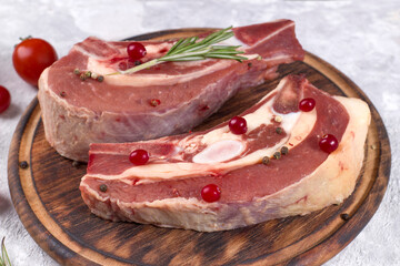 Several pieces of raw beef brisket on the bone with cranberries, rosemary and cherry tomatoes on a light background.