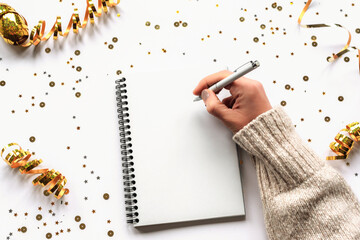 Woman's hand with pen writing in notebook on white table with Christmas decorations. Top view, flat...
