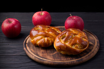 Obraz na płótnie Canvas Baked yeast buns with apple on wooden board on dark background