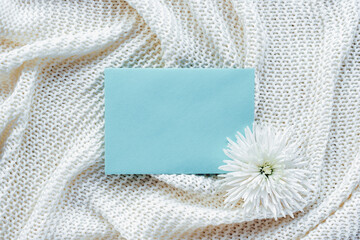 Blue envelope and chrysanthemum flower on white knitted plaid. Top view, flat lay. Mock up