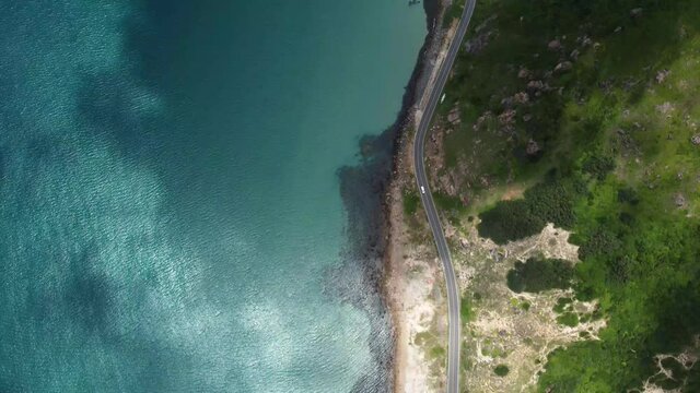 Top down view of curves of coastal road. Drone aerial view of the coastline. Tracking shot of the motorbike. Vehicles travelling along the shore. Trucks are going by the coast route. Con Dao, Vietnam.