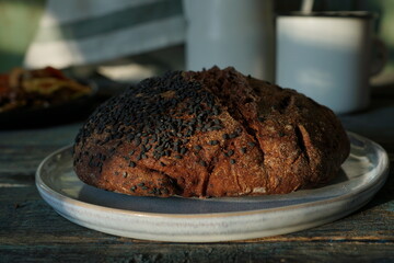 Round homemade bread, sprinkled with black sesame seeds, on a white ceramic plate. Homemade products.