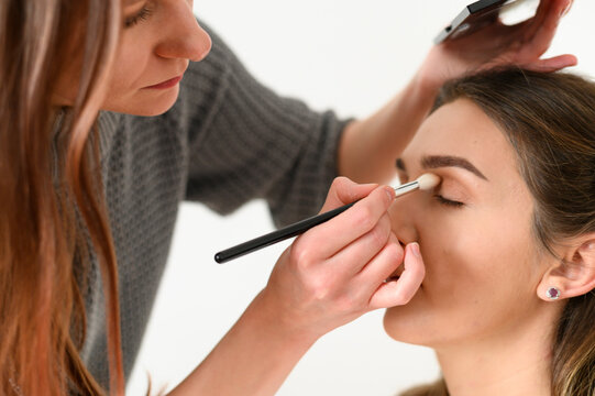 Close up portraits Makeup artist making professional makeup of smiling young woman. Makeup lessons
