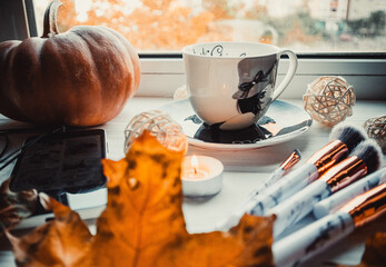 Cup of coffee with pumpkins on wooden white background with a makeup brushes in autumn. Flatlay