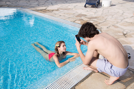 guy takes pictures of a beautiful young woman posing for him in the pool. Youth on vacation, having fun on vacation. Relationships, love, feelings between young adults