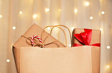 Paper bag with gifts wrapped in eco paper against golden background with bokeh. Winter holidays concept.