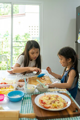 Asian girl in casual dress having fun while make pizza with prosciutto, tomato, cheese, vegetables in home kitchen. family and relationship concept