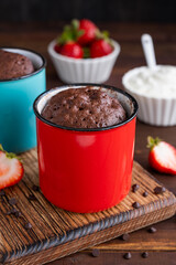 Chocolate mug cake with whipped cream and fresh berries on a dark wooden background. Cupcake cooked...
