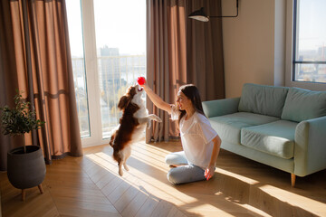 Woman playing with Cavalier King Charles Spaniel dog at home and smiling.