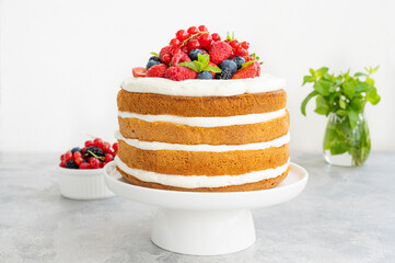 Homemade naked layered vanilla cake with whipped cream and fresh berries on top on a gray concrete background. Summer cake. Copy space.