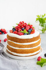 Homemade naked layered vanilla cake with whipped cream and fresh berries on top on a gray concrete background. Summer cake. Copy space.