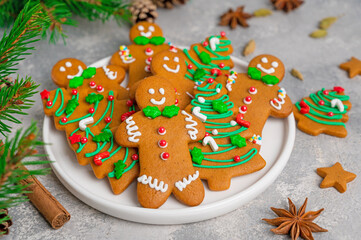 Gingerbread cookies in the form of man and christmas trees decorated with sugar glaze and sprinkled sugar candy on a plate on a gray concrete background. Pastries for Christmas and New Year.