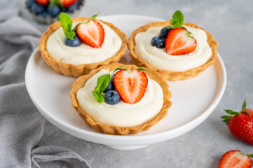 Delicious mini tarts with fresh berries and custard on a white plate on a gray concrete background. Copy space