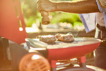 Close up on man's hand seasoning meat on the gas grill on barbecue grill outdoor