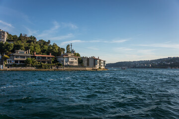 Luxurious houses and mansions over the hills located on the shore of Istanbul Bosphorus strait with green trees on the back and blue water in front of the houses.