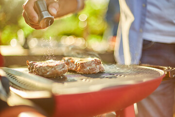 Close up on man's hand seasoning meat on the gas grill on barbecue grill outdoor