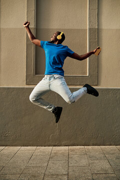Energetic black man with headphones jumping on street