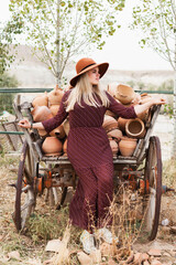 Young woman wearing hat and dress near  pottery Jugs from wooden rural cartload. Slow living lifestyle concept. Cappadocia travel adventures.