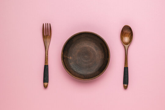 Wooden spoon and fork and clay bowl on pink background. Vintage tableware.