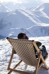 Skier at winter mountains resting on sun-lounger at nice sun day