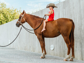 Small boy in cowboy hat sitting on brown horse