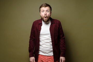 Handsome bearded man is amazed, he opens mouth in surprise and looks with big eyes. Green...